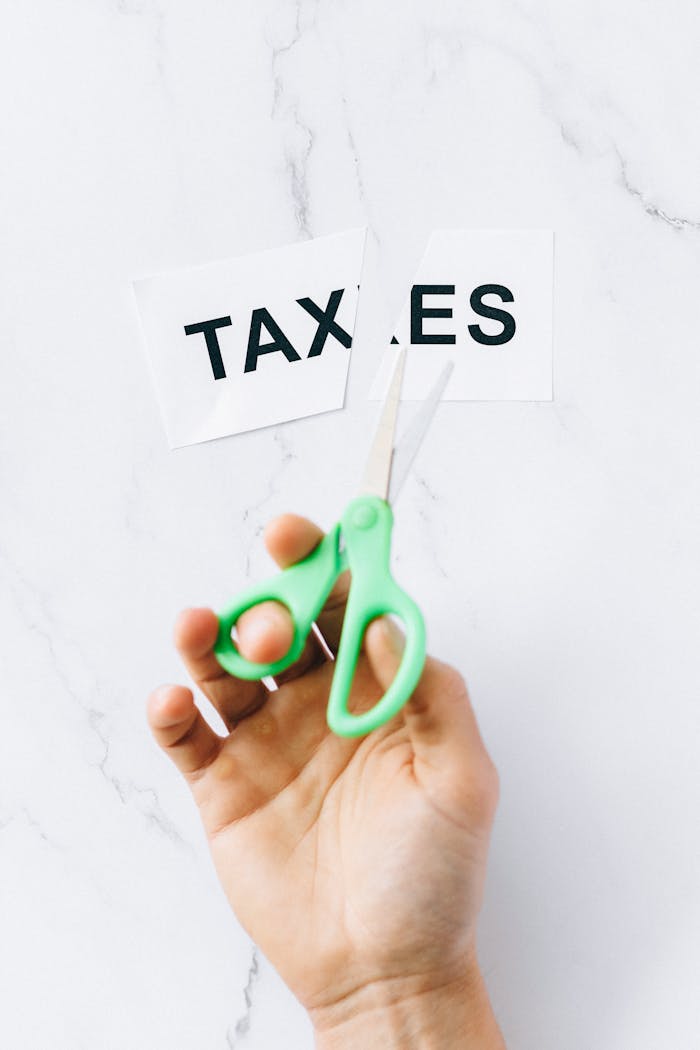 Top-down view of a hand holding scissors cutting the word taxes on a marble surface.